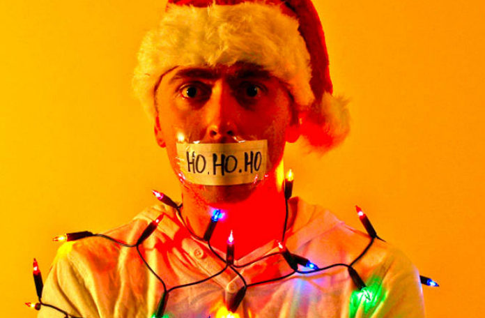 Mężczyzna w czapce Mikołaja z zaklejonymi ustami i obwiązany świątecznymi lampkami