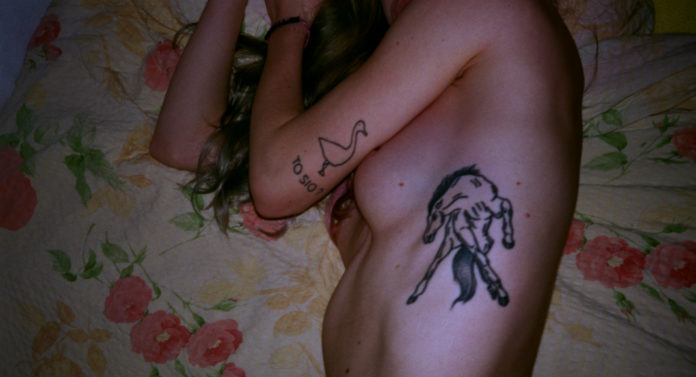Dziewczna leżąca na łóżku z zakrytymi piersiami i tatuażem konia na wysokości żeber