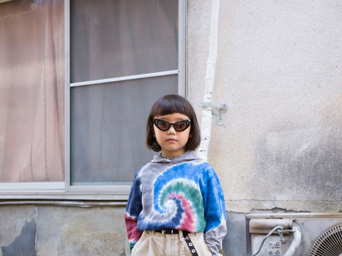 Dziecko, japonka, stojąca w środku kadru, ubrana w okulary przeviwsłoneczne i kolorową bluzkę