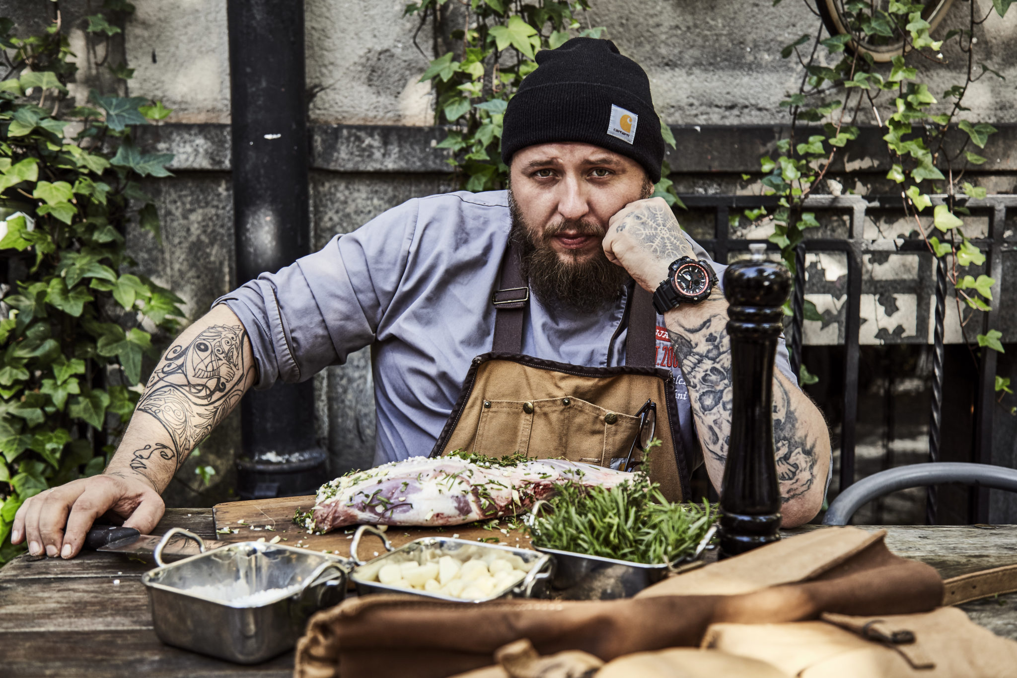 Mężczyzna z tatuażami i czapką na głowie siedzący przy stole z jedzeniem