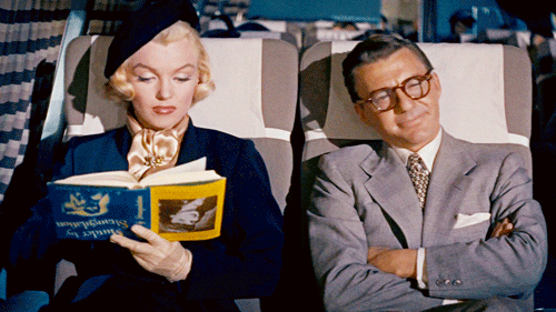 MarilynMonroe czyta książkę do góry nogami, obok siedzi mężczyzna