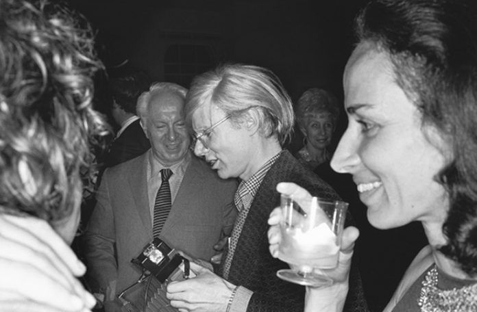 Czarno-białe zdjęcie przedstawiające mężczyzne trzymajacego aparat i kobiety ze szklanką przy ustach