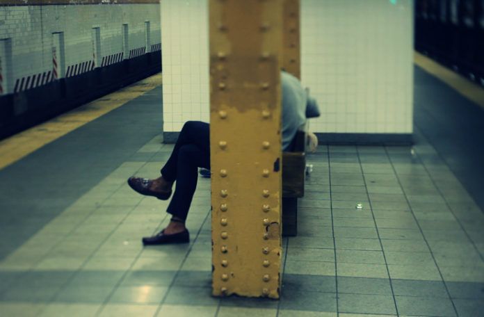 Człowiek siedzący na stacji metra z twarzą zasłoniętą przez barierkę