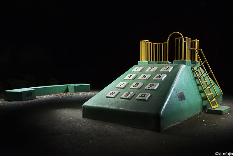 Duży, betonowy element placu zabaw w formie zielonego, starego telefonu stacjonanego i słuchawki.