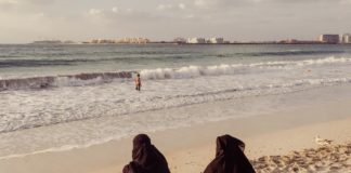 Dwie ubrane na czarno kobiety siedzące nad brzegiem morza