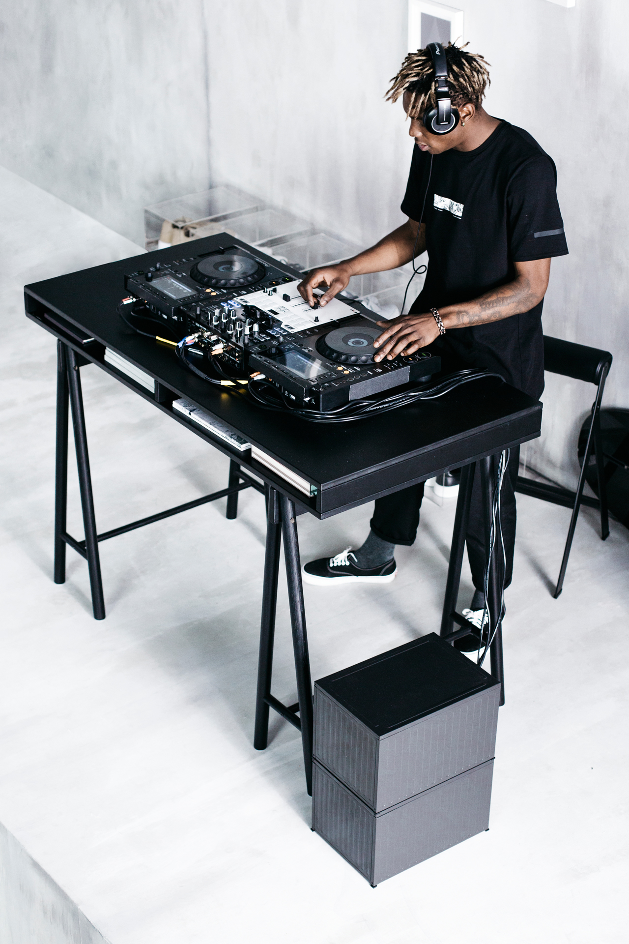 Mężczyzna w czarnym ubraniu grający jako DJ. Konsola na czarnym biurku.