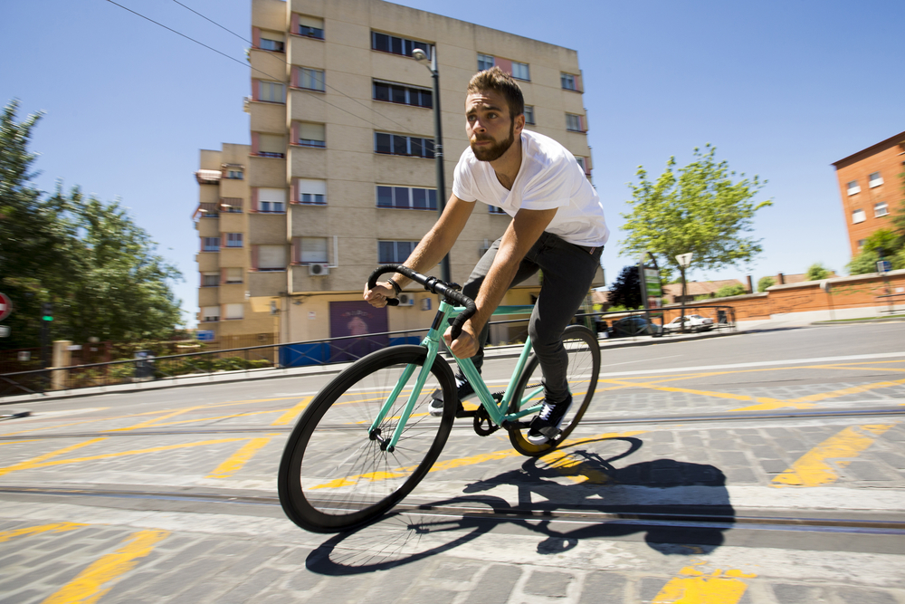 Mężczyzna jadący na rowerze ostrokołowym, w tle bloki