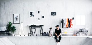 Mężczyzna w czarnym stroju siedzi obok psa w jasnym, minimalistycznym wnętrzu.