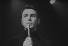 Czarno-biały kadr prezentujący mężczyznę z mikrofonem w dłoni