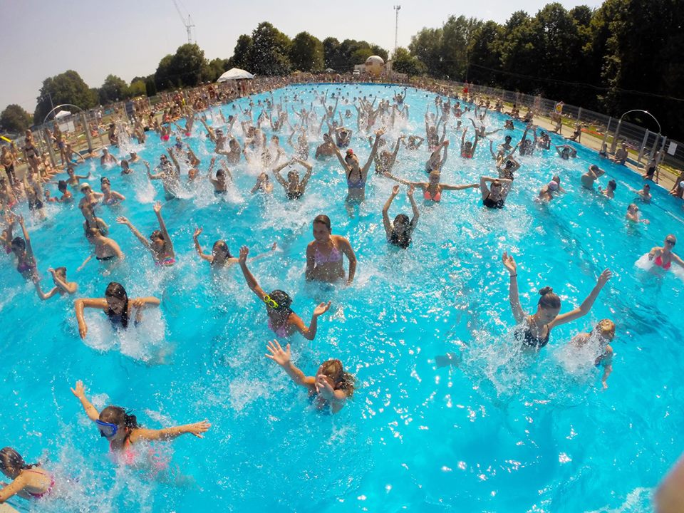 Tłum rozbawionych dzieci w basenie z błękitną wodą.