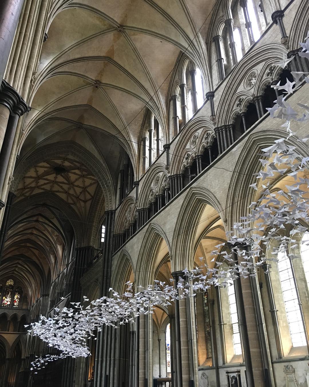 Białe papierowe gołębie zawieszone pod sklepieniem gotyckiego kościoła.
