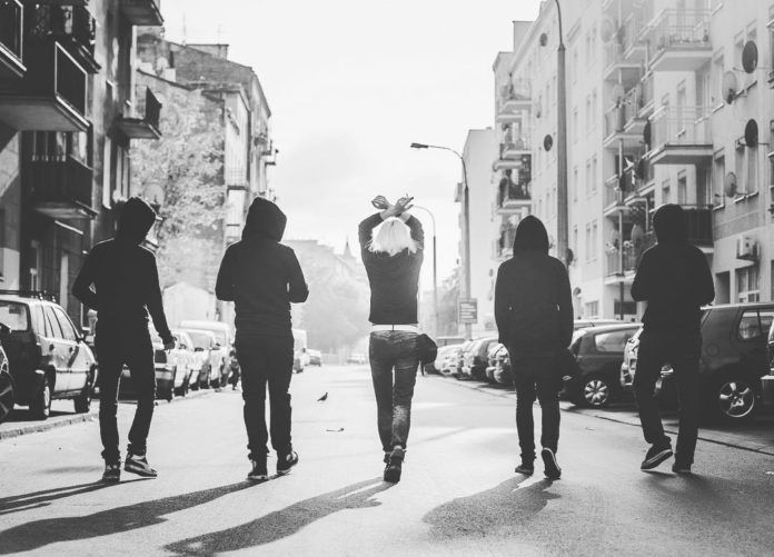Czarno-biale zdjęcie przedstawiające cztery osoby idące tyłem do ulicy