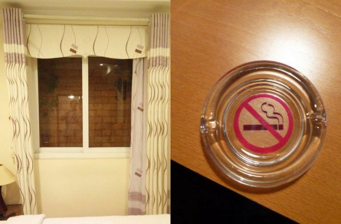 Okno za którym widać ścianę z cegieł i popielniczka z zakazem palenia