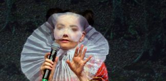 Kobieta w ekscentrycznym przebraniu z białą woalką na głowie z mikrofonem w ręce.