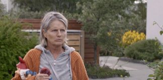Kobieta ubrana w dres stoi przed domem i trzyma w ręku dwa krasnale ogrodowe