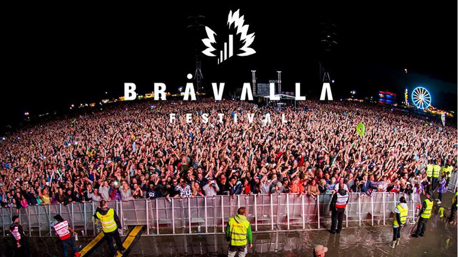 Zdjęcie publiczności na festiwalu Bråvalla w Szwecji. Ludzie odgrodzeni barierkami i kordonem ochrony. 