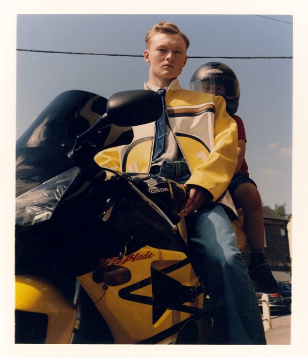 młody mężczyzna siedzi na żółtym motorze w skórzanej kurtce, za nim siedzi młody chłopiec w kasku