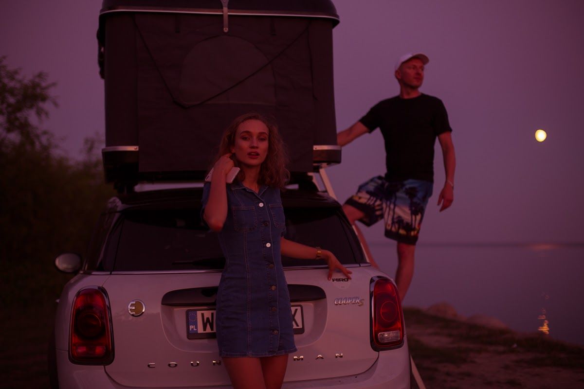Samochód z namiotem na dachu, dziewczyna w jeansowej sukience i mężczyzna z boku samochodu
