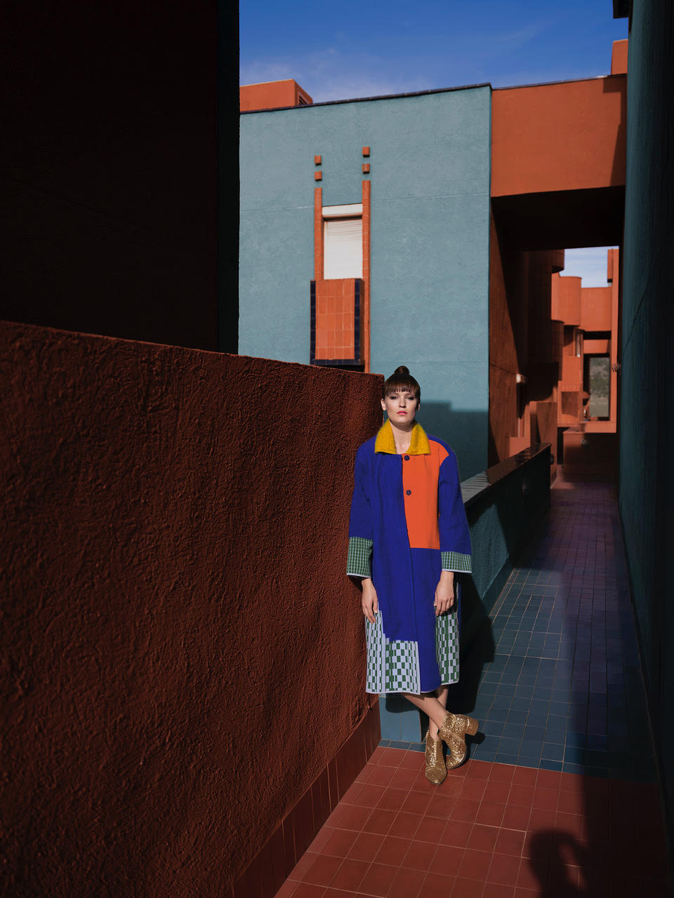 Mloda kobieta pozuje w kolorowej sukience na tle niebieskiego budynku