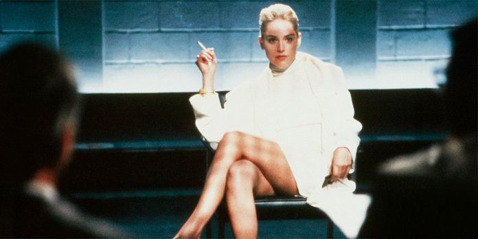 Blondynka ubrana w białą sukienkę i biały płaszcz pali papierosa i siedzi ze skrzyżowanymi nogami