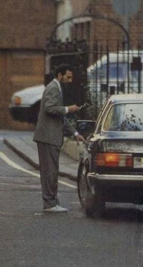 zdjęcie przedstawiające Frediego Mercurego z papierosem w garniturze przy samochodzie
