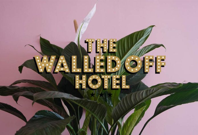 Napis The Walled Off Hotel z rośliną i różowym tłem