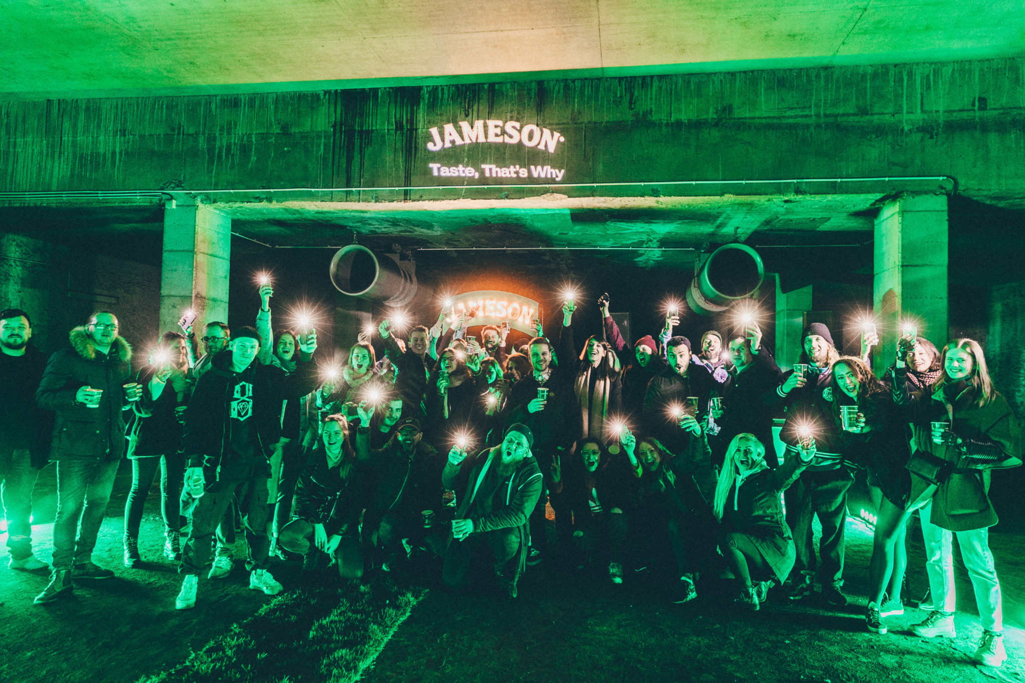 Grupa ludzi pozująca do zdjęcia w ciemnym pomieszczeniu oświetlonym na zielono