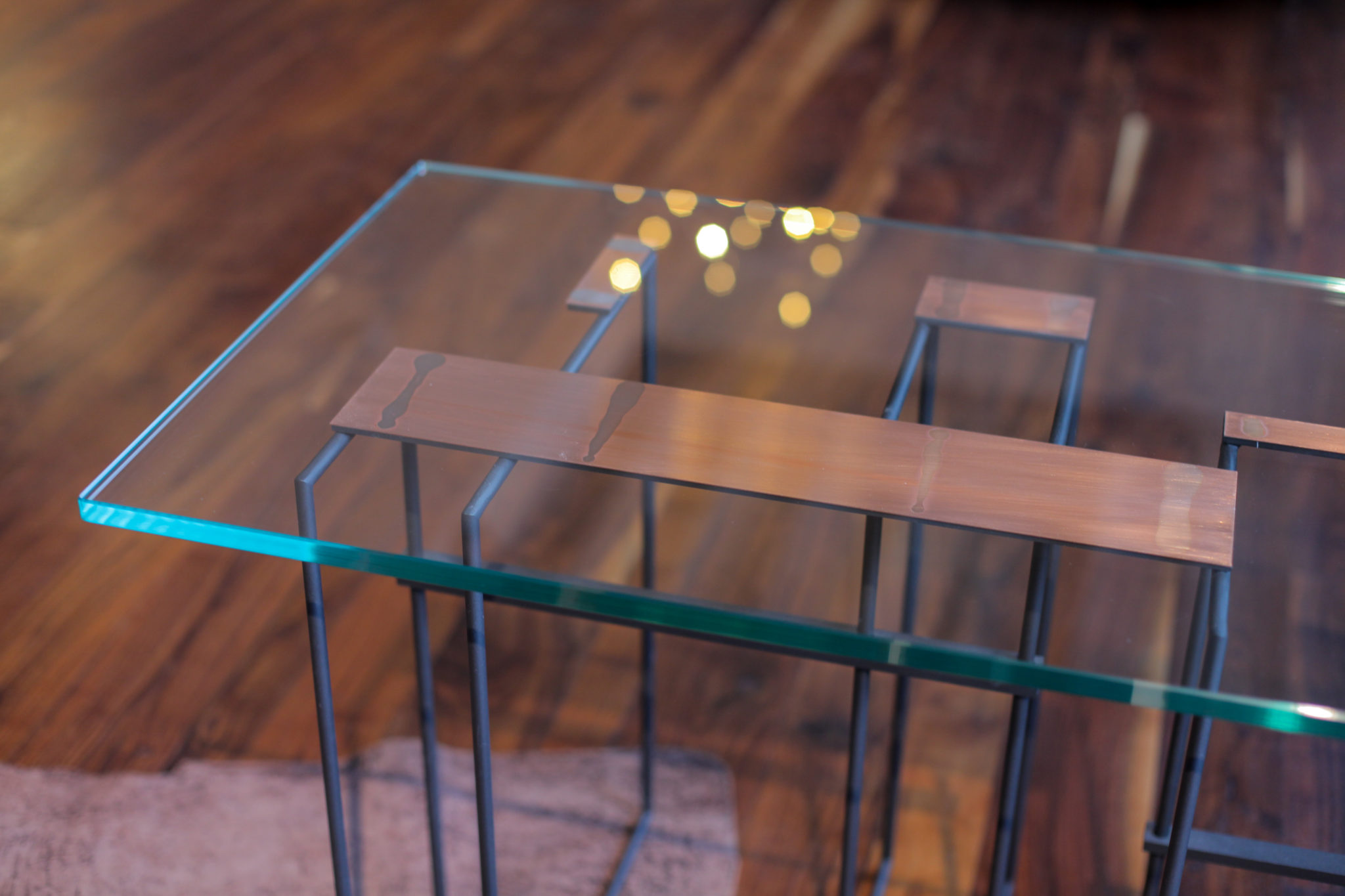 Szklany stolik z miedzianymi elementami na drewnianej podłodze