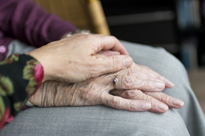 zdjęcie ukazuje dłoń starszej osoby, na której młoda osoba trzyma swoją rękę 