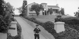 Czarno-białe zdjęcie pokazujące policjanta stojącego przed willą