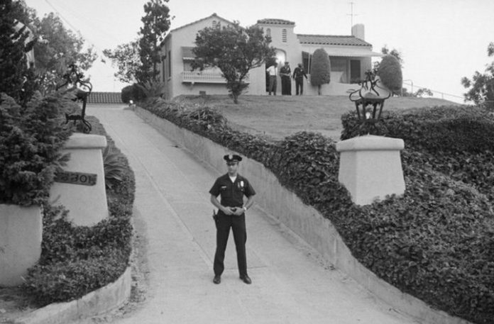 Czarno-białe zdjęcie pokazujące policjanta stojącego przed willą