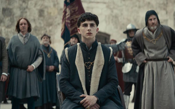 Kadr z filmu The King, w centrum siedzi ubrany w średniowieczny strój Timothee Chalamet, grający główną postać księcia Hala