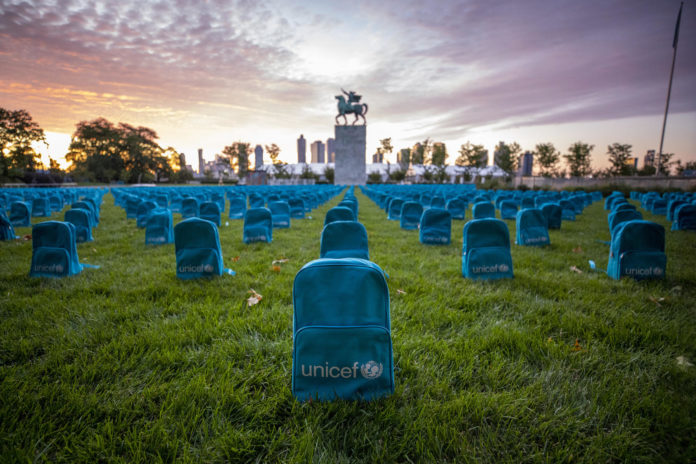 Błękitne plecaki z logo UNICEF, ustawione rzędami na polanie.