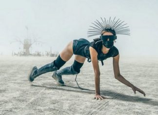 kobieta w czarnym stroju z kolcami na głowie oraz w masce na pustyni