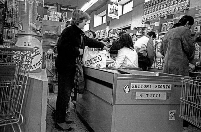 Czarno-białe zdjęcie przedstawiające kobietę przy kasie sklepowej