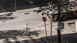 Człowiek ubrany w biały kombinezon ochronny dezynfekuje ulicę z gumowego węża