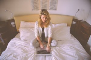 Dziewczyna siedzi w siadzie skrzyżnym na łożku i pracuje z laptopem