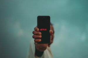 Mężczyna trzyma w ręku smartphone na którym widać napisać logo Netflix