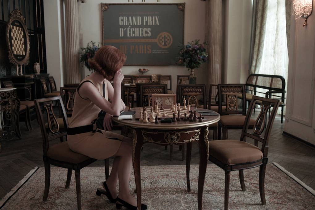 Młoda dziewczyna siedzi i patrzy na szachy, ktore sa na stoliku